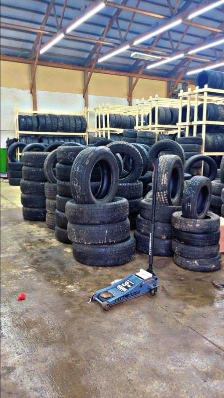 Stacks of used tires with a floor jack in front of the tire racks